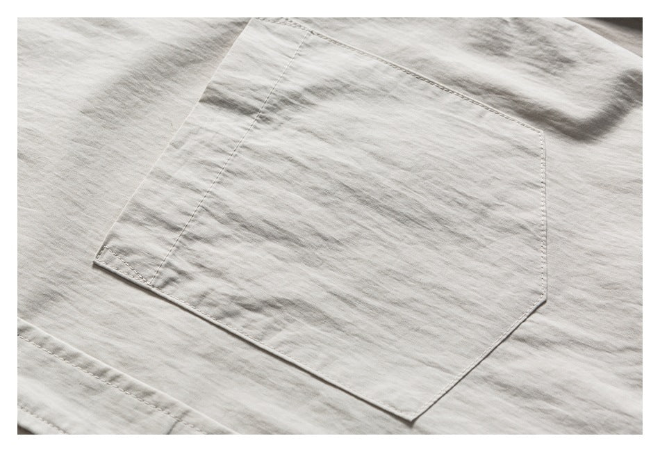 Close-up of a large stitched patch pocket on an off-white garment.