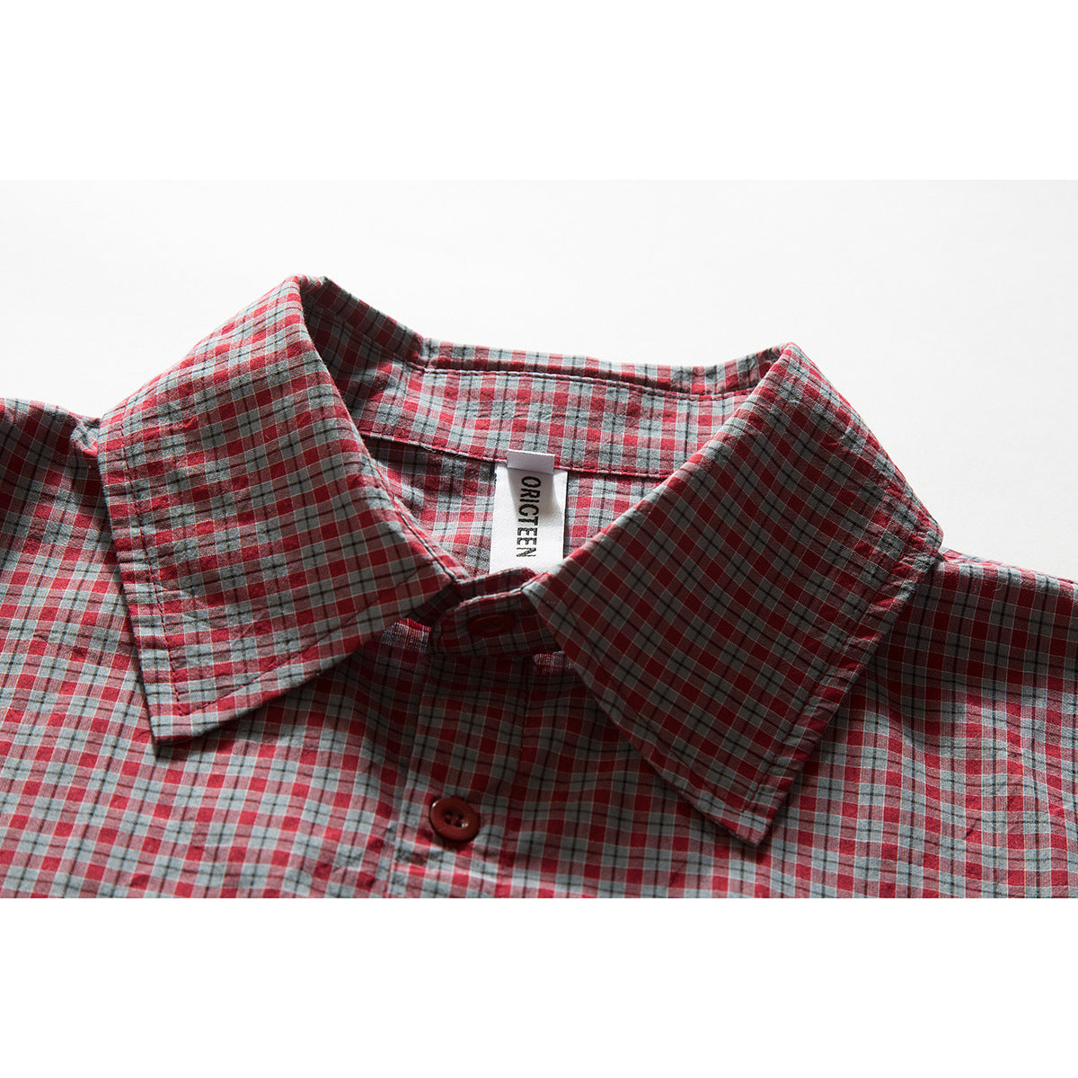 Close-up of a red, gray, and blue plaid shirt collar, button, and sewn neck label.