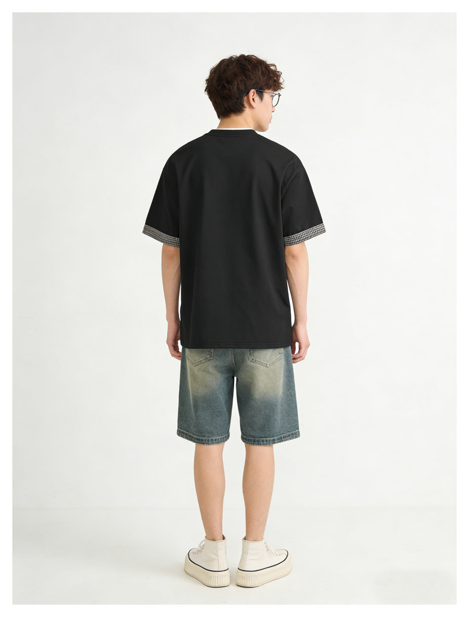 Back view of a model wearing a black T-shirt with checked sleeve cuffs and blue denim shorts.