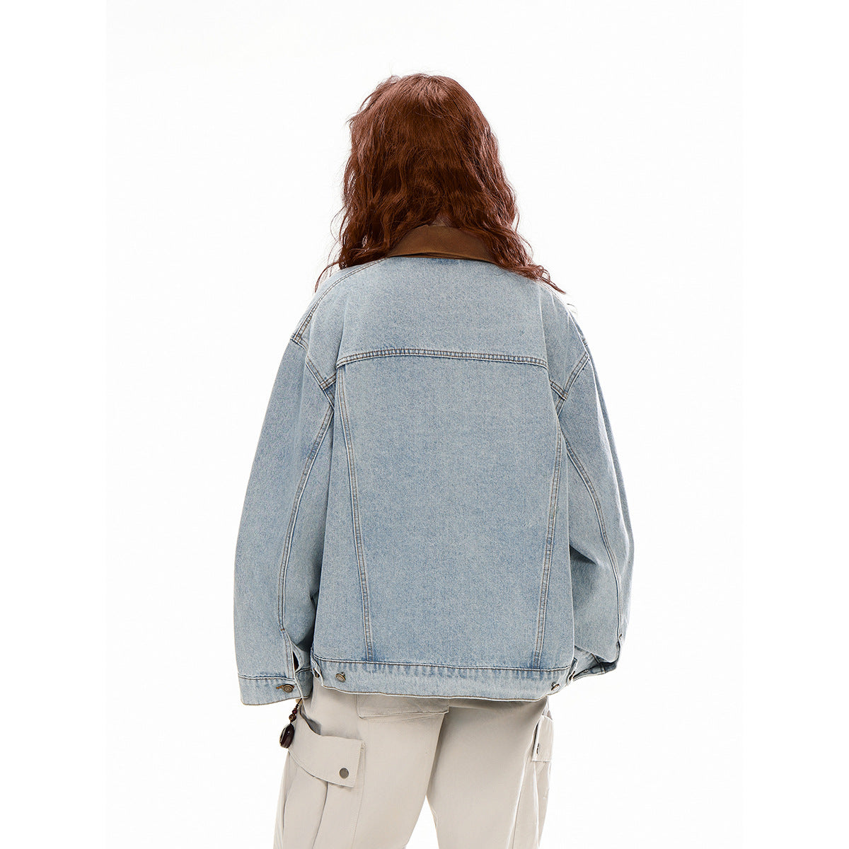 Rear view of a model wearing an oversized light-wash denim jacket with a brown collar and beige cargo pants.
