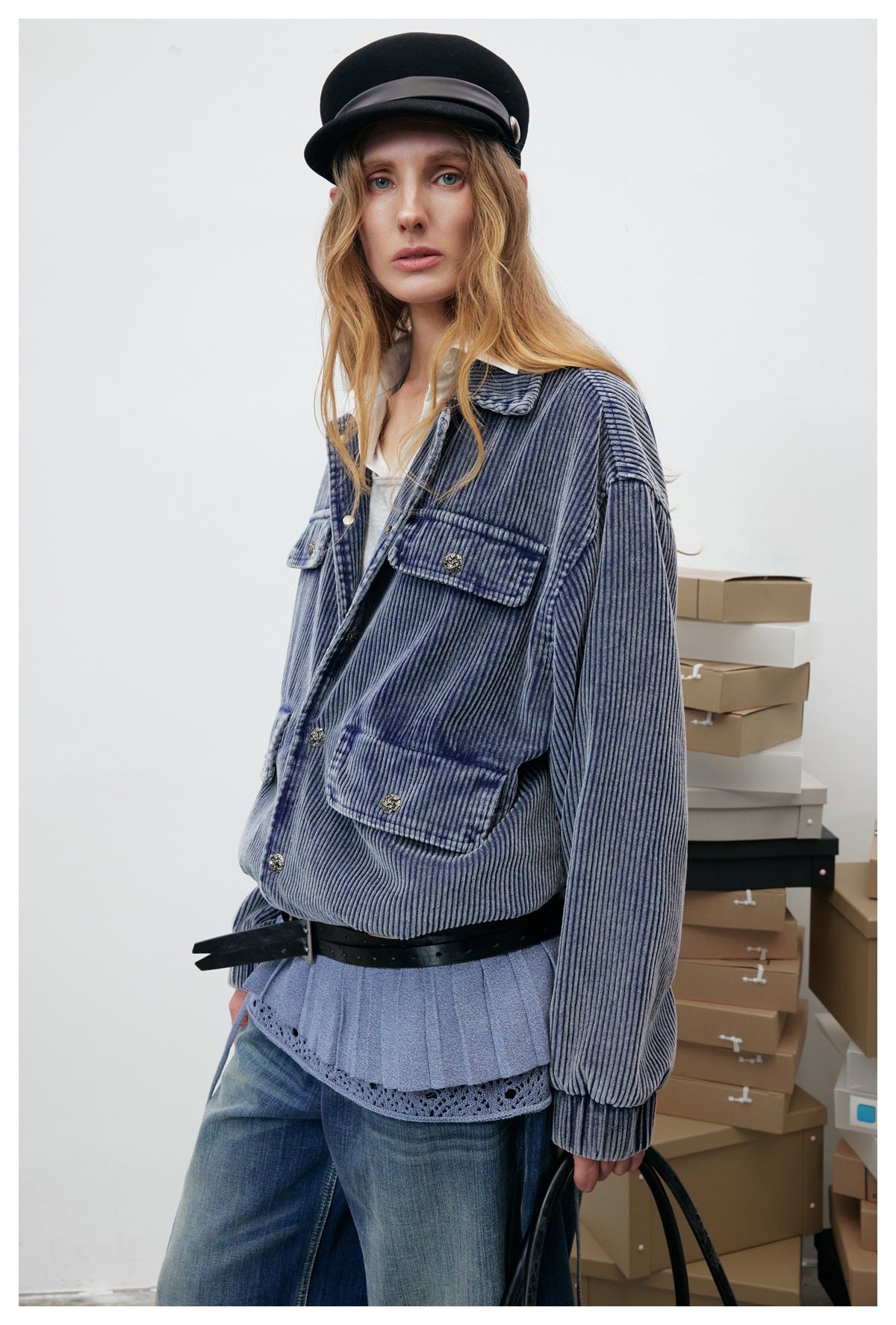Three-quarter view of a model wearing a blue-gray ribbed jacket with a pointed collar and four flap pockets.