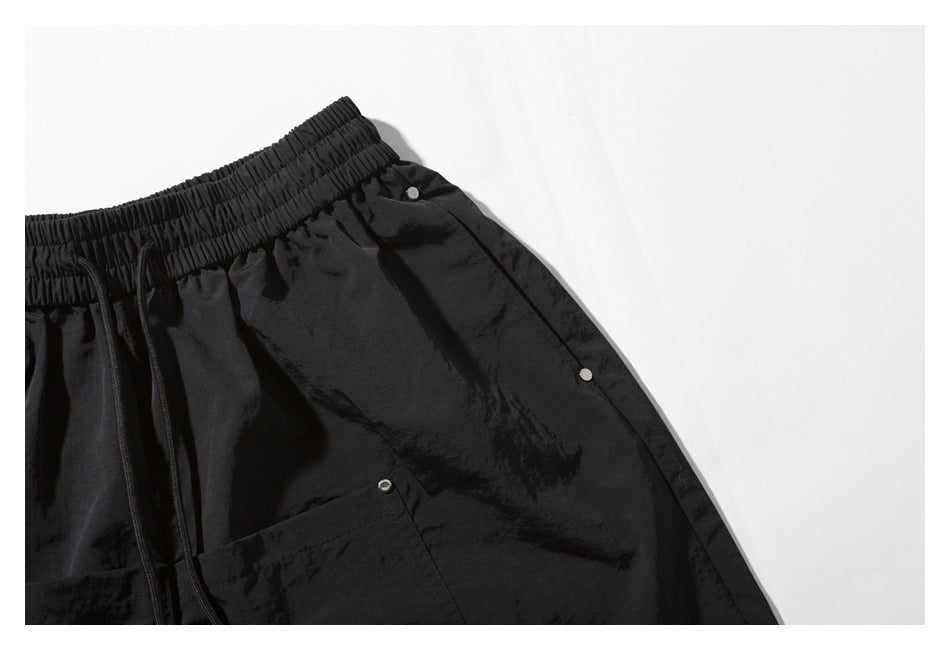Close-up of black shorts showing the gathered elastic waistband, drawstring, and snap-fastened side detail.