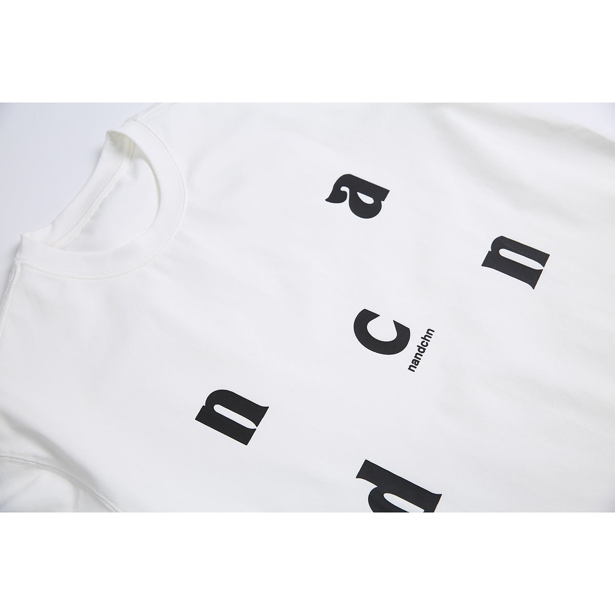 Close-up of a white T-shirt with scattered black letters and small “nandchn” text.