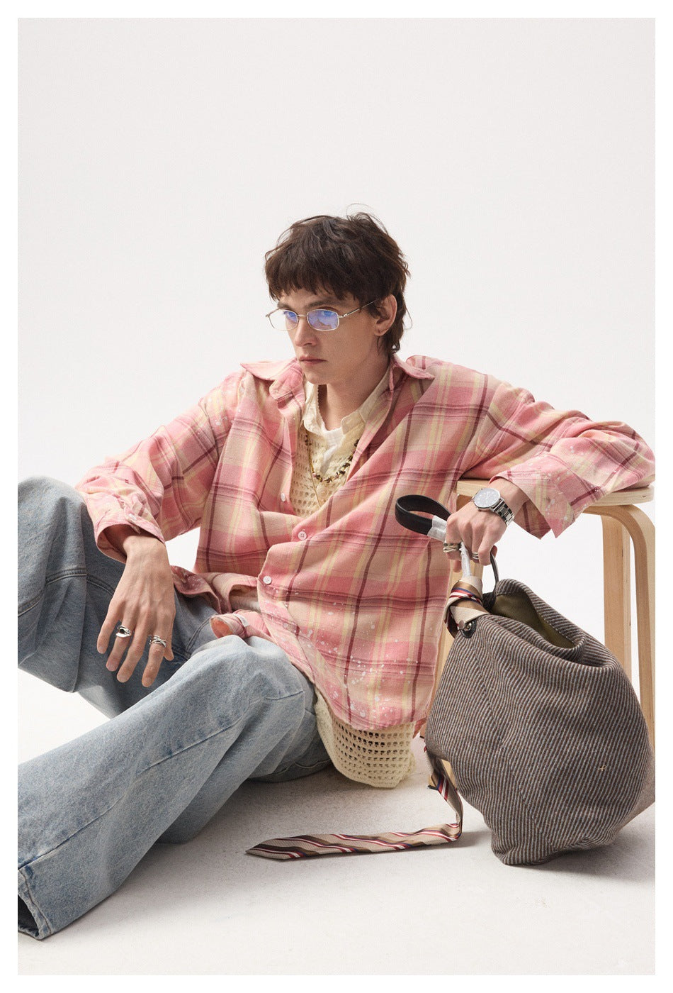 Model seated in a pink plaid button-up shirt with white splatter details and light jeans.