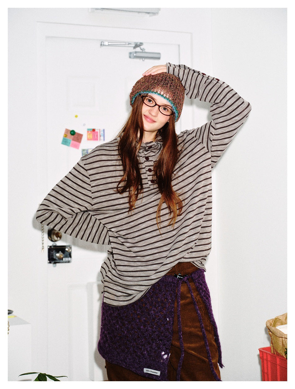 Woman wearing the striped stand-collar button-placket top with one arm raised, styled with a knit beanie and skirt