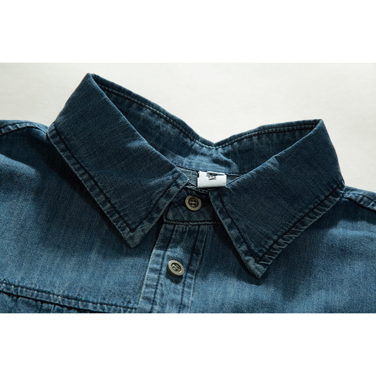 Close-up of a dark blue denim shirt collar, top buttons, and shoulder seams.