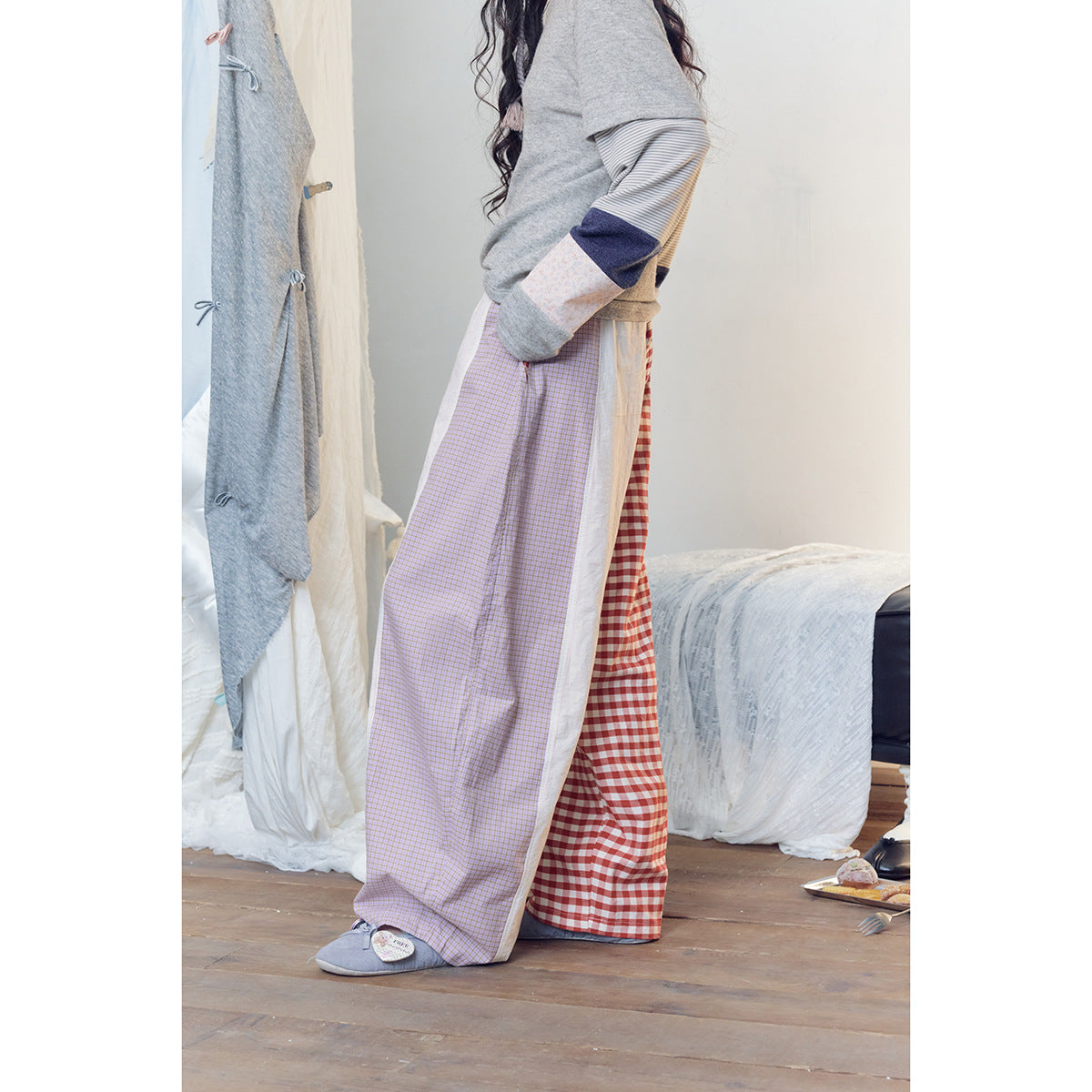 Side view of a model wearing wide patchwork trousers, showing lilac checks and red gingham panels.