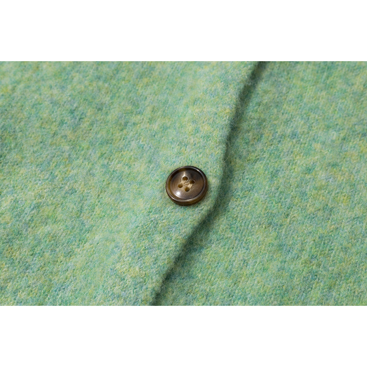 Close-up of a dark brown four-hole button on mottled mint green knit fabric.