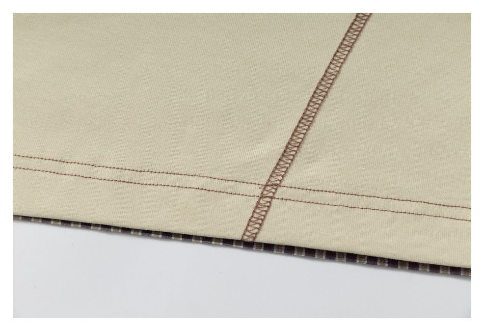 Close-up of brown stitching along the hem and seam of cream fabric, with a narrow plaid edge underneath.
