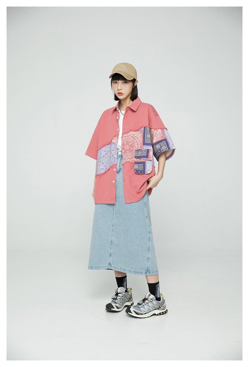 Model wearing an oversized coral short-sleeve shirt with patchwork paisley panels, shown from the front at an angle.