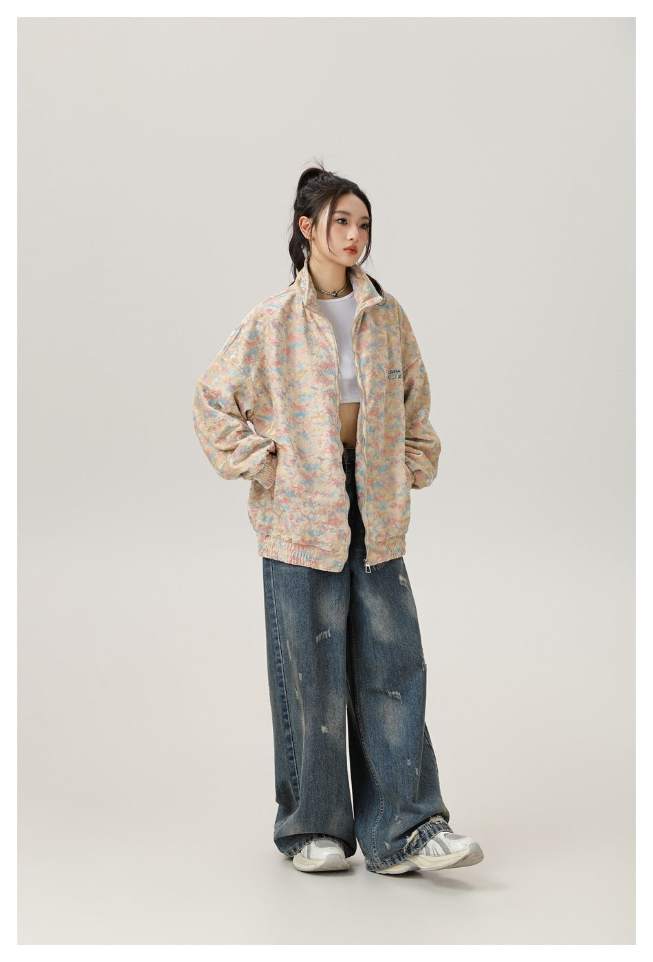 Model wearing a pastel multicolor zip-up jacket with a high collar and elastic cuffs, paired with wide-leg distressed jeans.