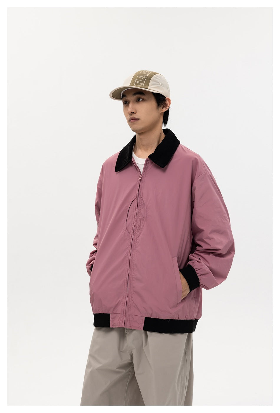 Man in pink zip jacket with black collar and ribbed hem, hand in pocket, three-quarter view