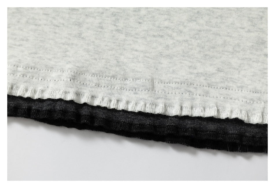 Close-up of a light gray heather garment hem with a black layer beneath it.