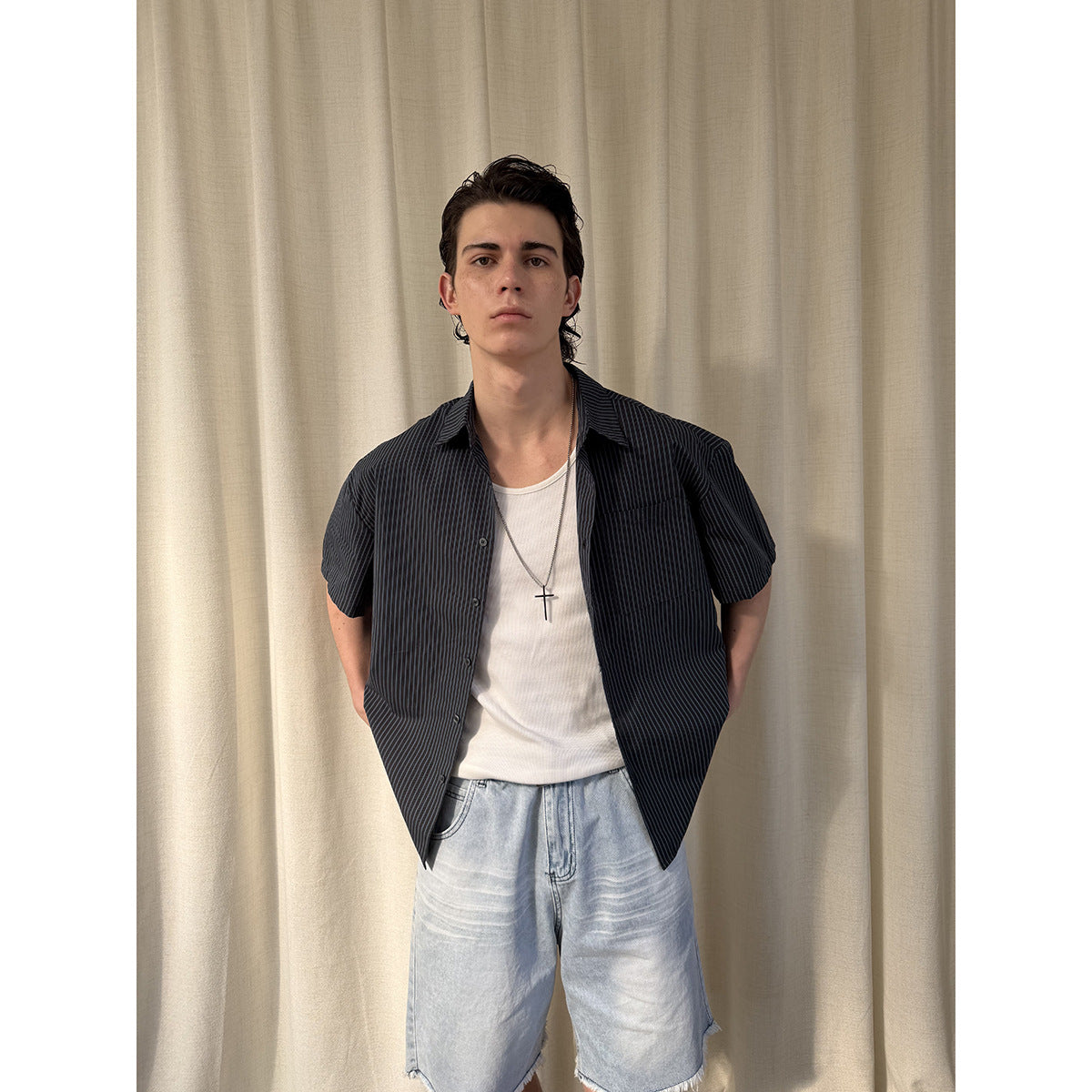 Closer front view of a model in a dark pinstriped short-sleeve shirt, white tank, and light blue denim shorts.
