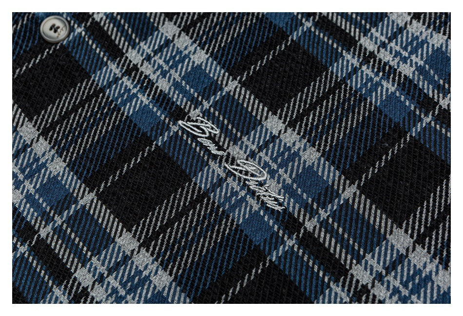 Close-up of embroidered script and a button on blue, black, and white plaid shirt fabric.