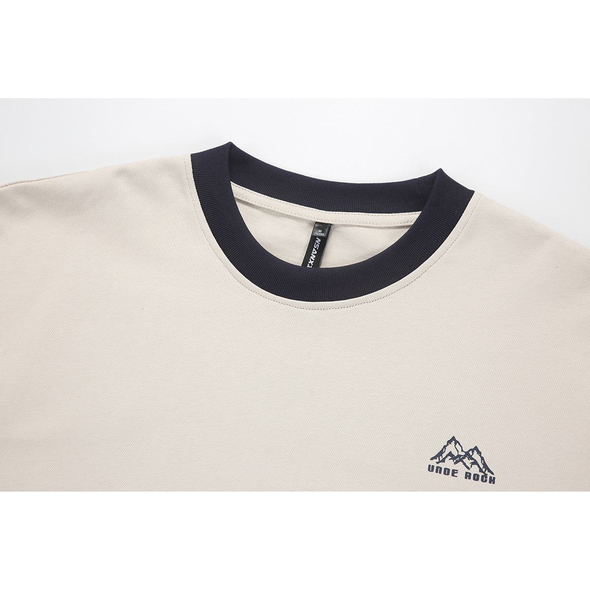 Close-up of a cream T-shirt with a dark navy ribbed crew neck and small mountain logo on the chest.