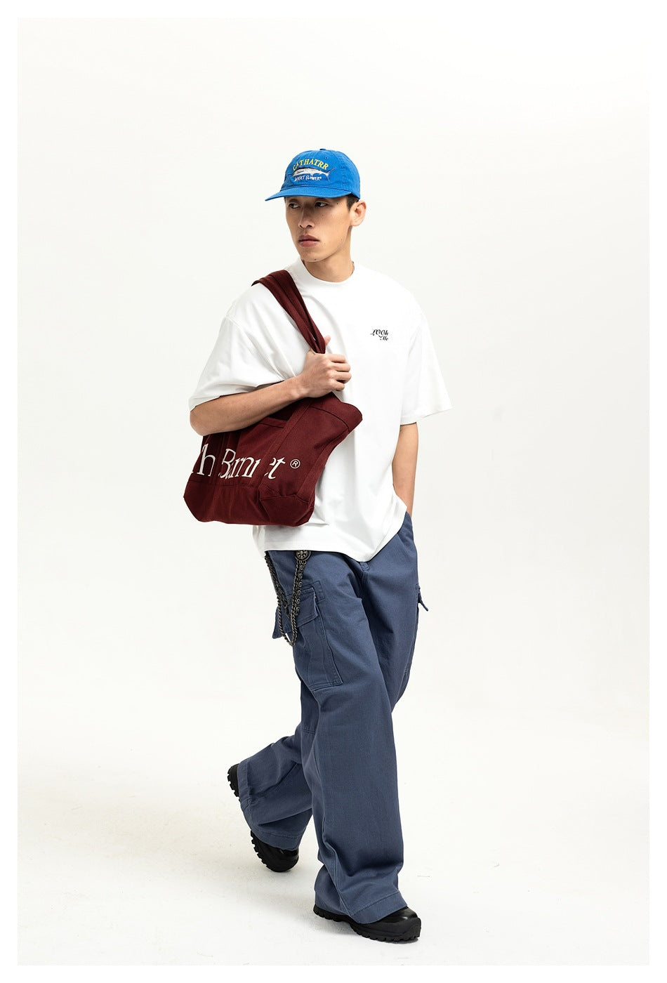 Model wearing an oversized white T-shirt with small black chest lettering and loose blue cargo trousers.