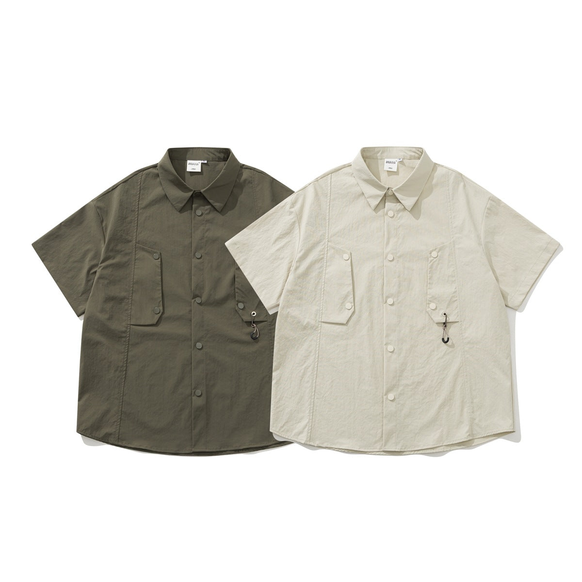 Front view of two short-sleeve button-up shirts, one dark olive and one ivory, with flap pockets and hook accents.