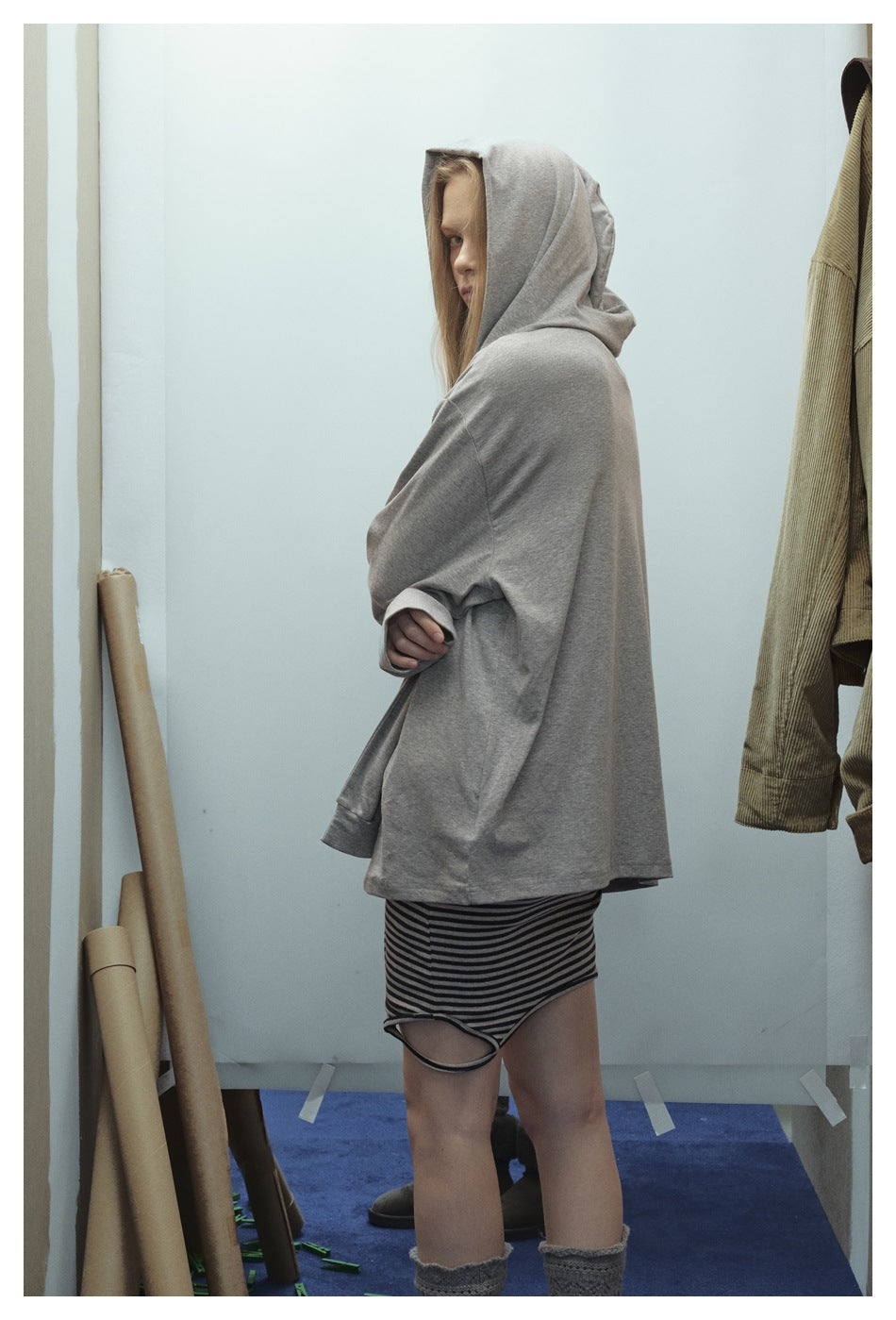 Side view of a model wearing a loose gray hooded top and a black-and-gray striped skirt.