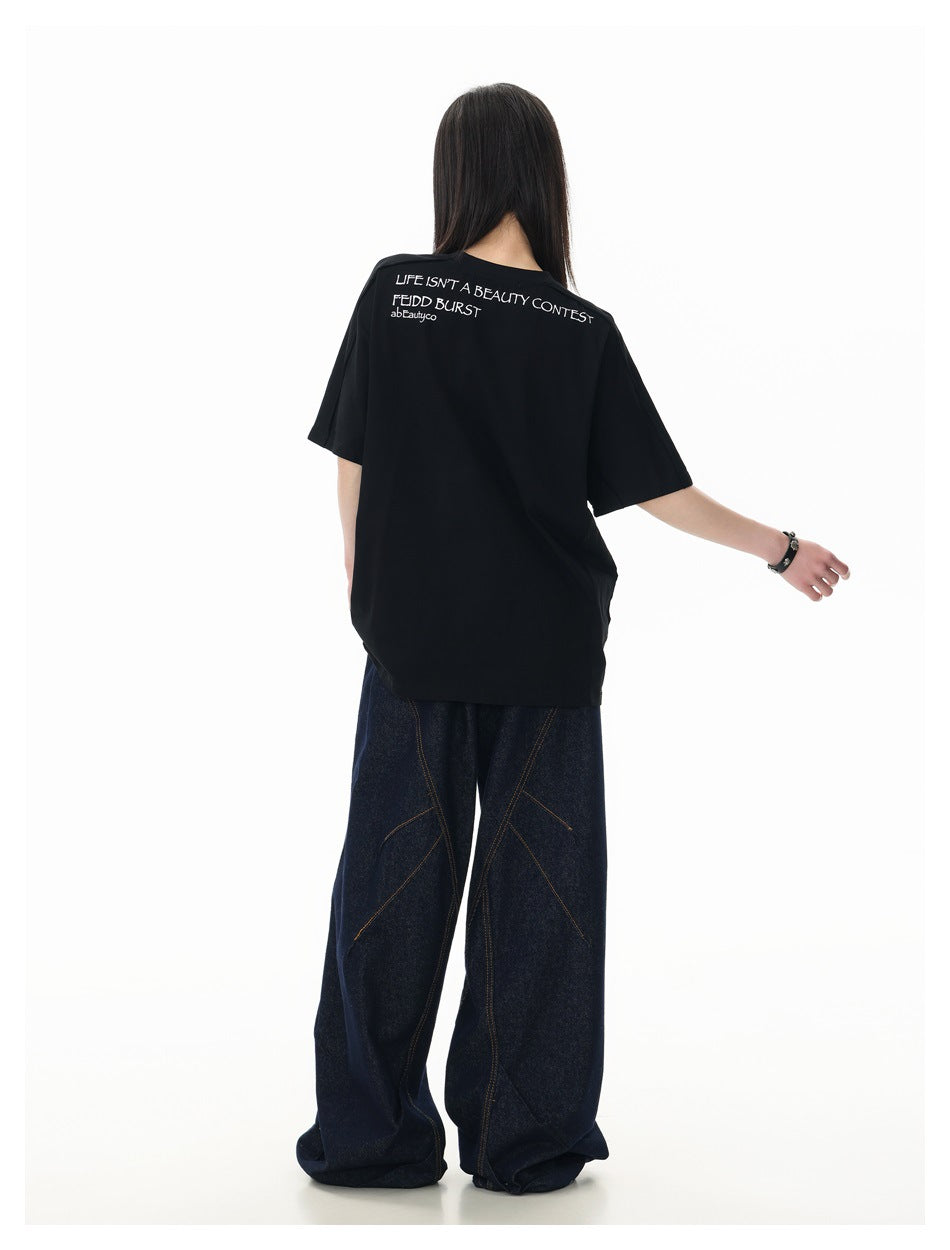 Rear view of a model wearing a black oversized T-shirt with white upper-back lettering and dark wide-leg jeans.