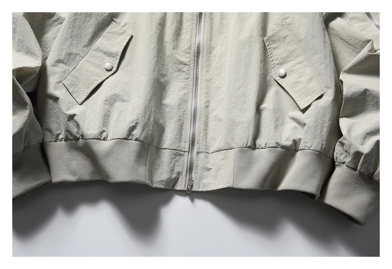 Cropped front view of a light stone-gray jacket with a central zipper, flap pockets, and ribbed hem and cuffs.