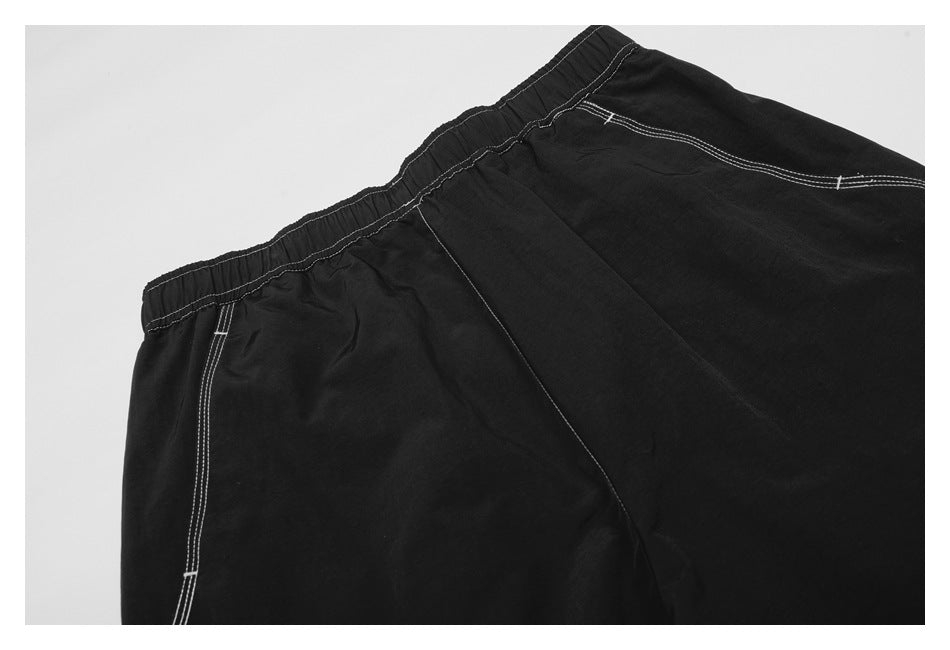 Close-up of black trousers showing an elastic waistband and white-stitched seams.