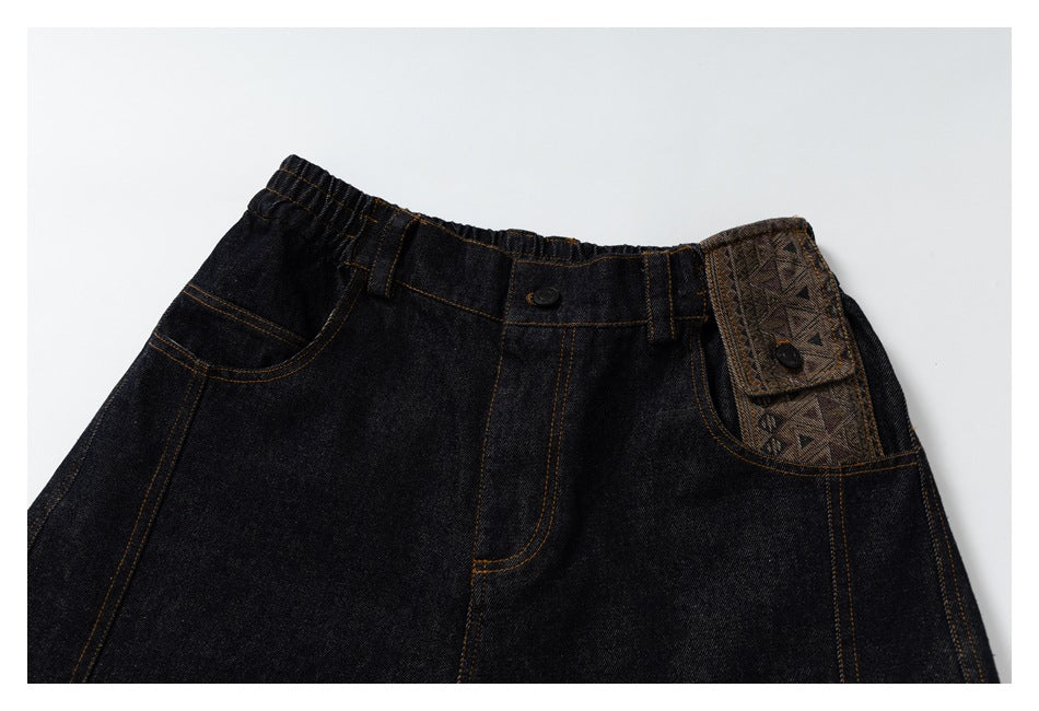 Close view of dark jeans showing the waistband, front pockets, contrast stitching, and patterned pocket flap.