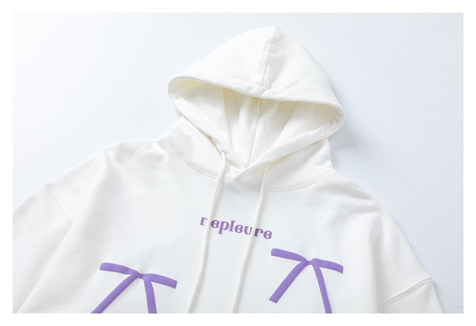 Cropped front view of a white hoodie with a hood, drawstrings, purple lettering and bow graphics.