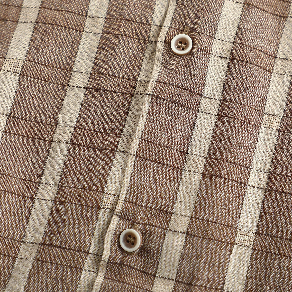 Close-up of the brown and cream plaid shirt fabric, front placket and two buttons.