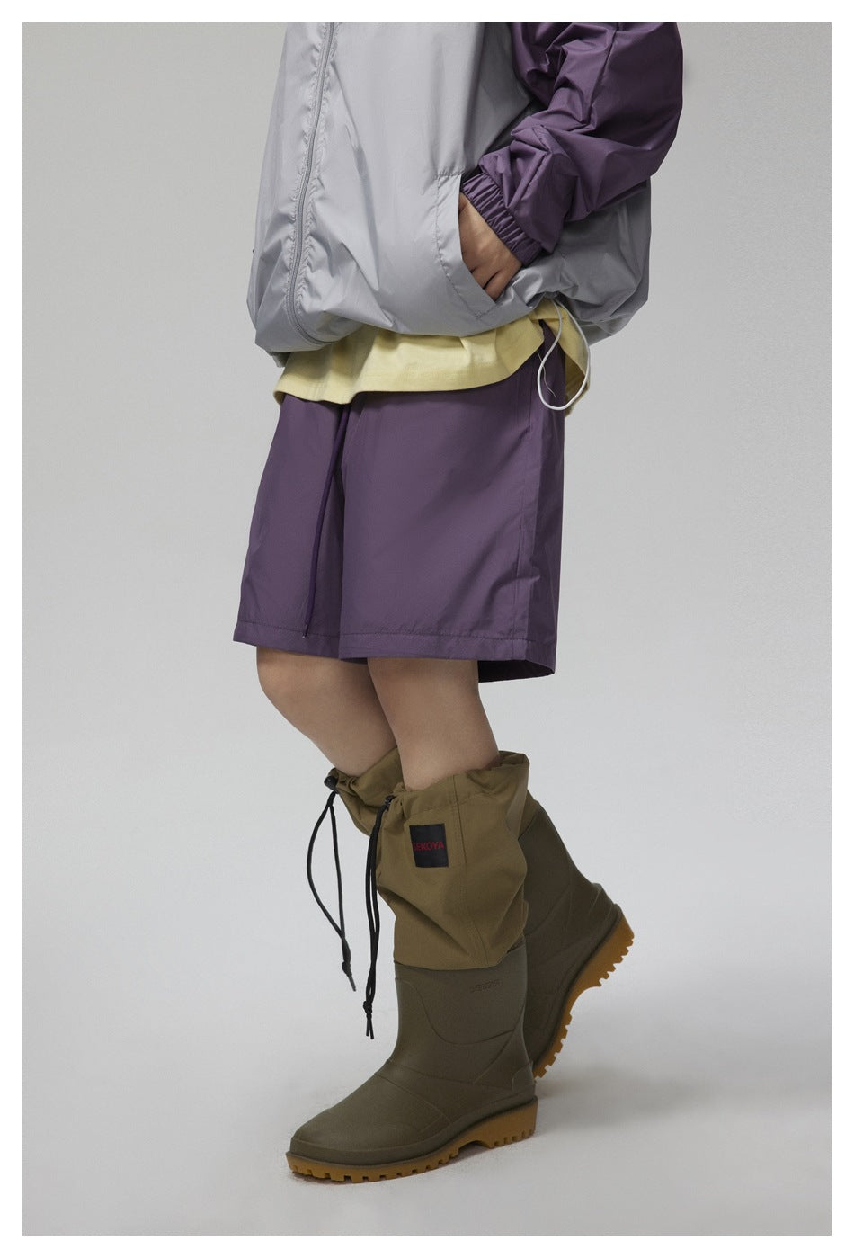 Close-up of purple shorts beneath a gray-and-purple jacket, with olive rain boots and gathered gaiter covers.