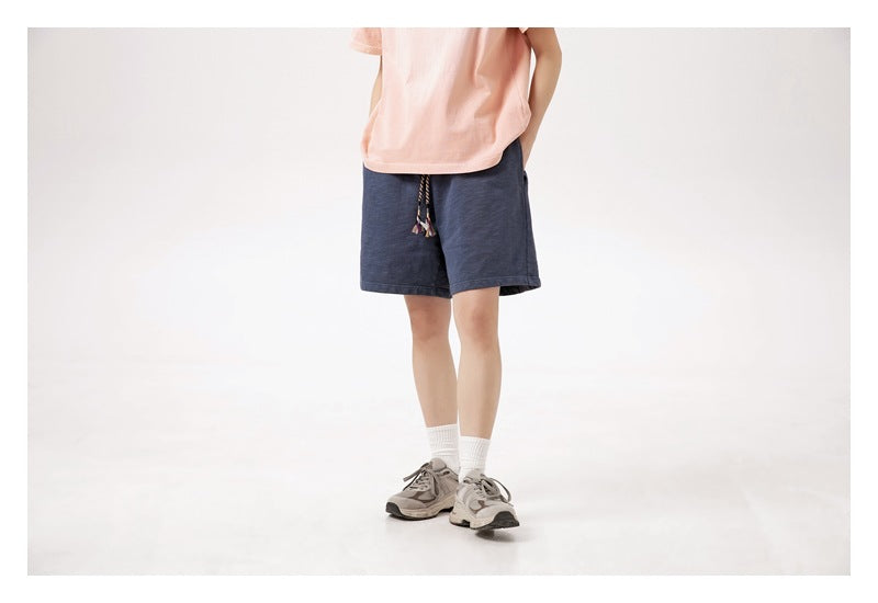 Cropped view of a model wearing navy drawstring shorts with a peach T-shirt, white socks and sneakers.