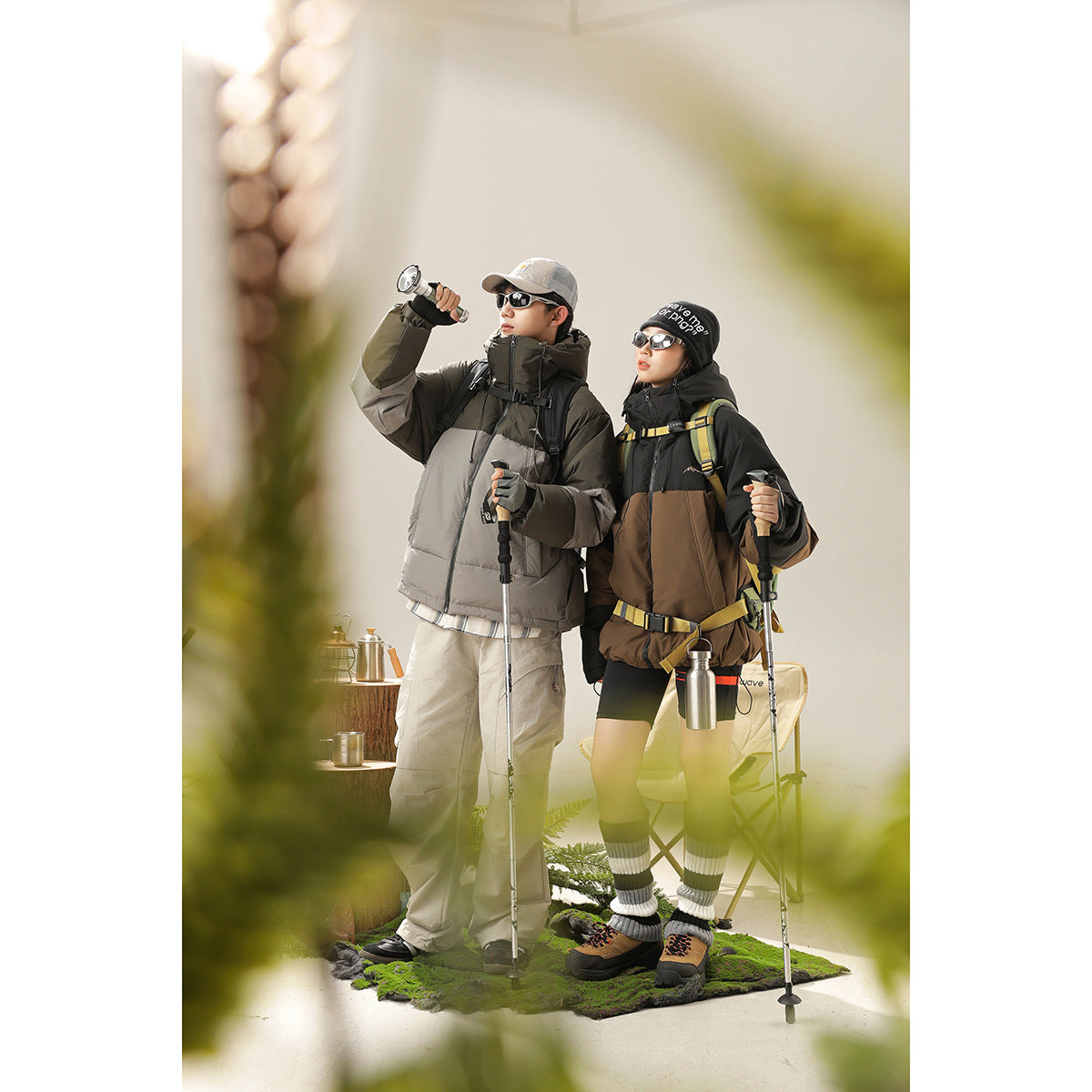 Two hikers model a gray and olive or black-and-brown color-block hooded jacket with trekking gear.