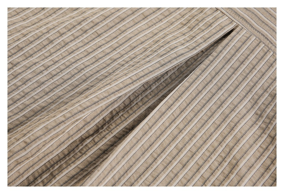 Close-up of beige fabric with narrow dark and light stripes, gathered into a diagonal fold.