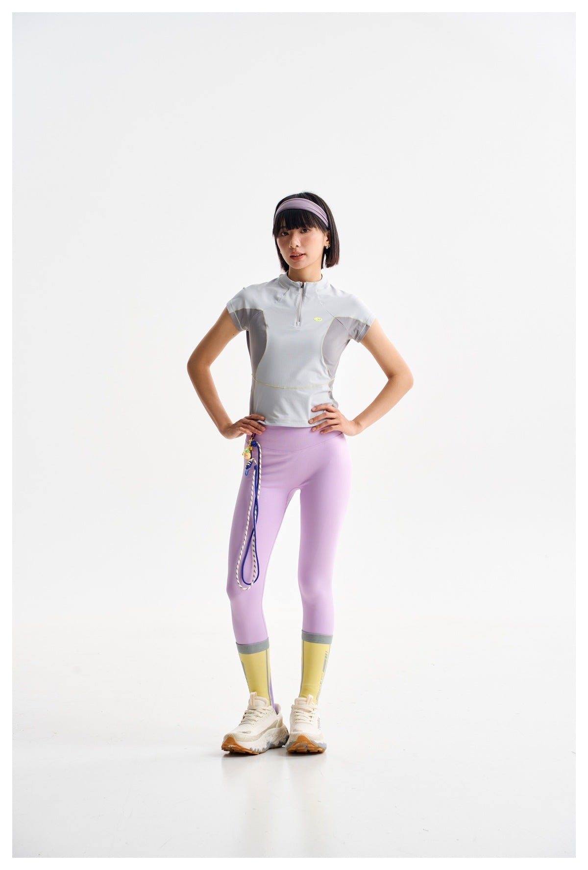 Front view of a model in a light gray zip-neck top, lavender leggings, and yellow leg warmers.