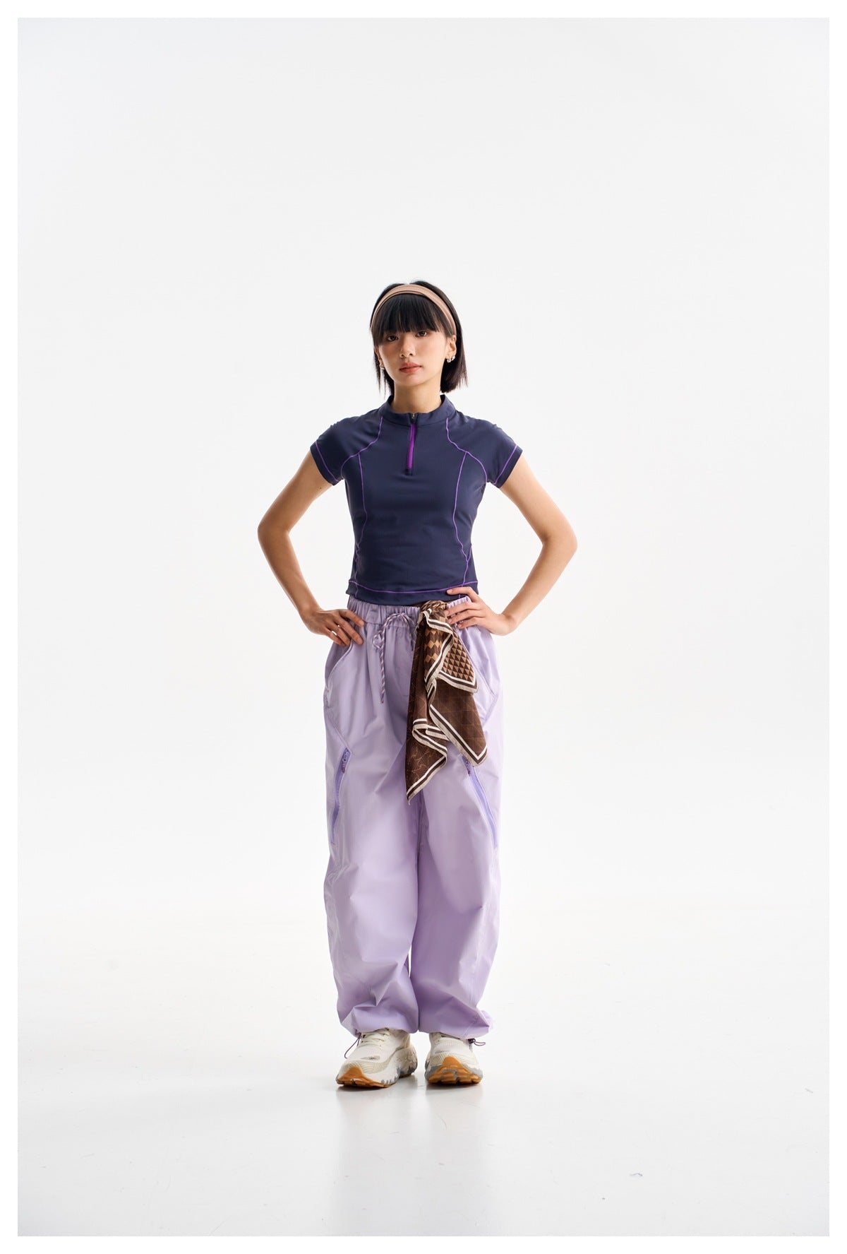 Front view of a model in a navy short-sleeve zip-neck top with purple piping and loose lavender pants.