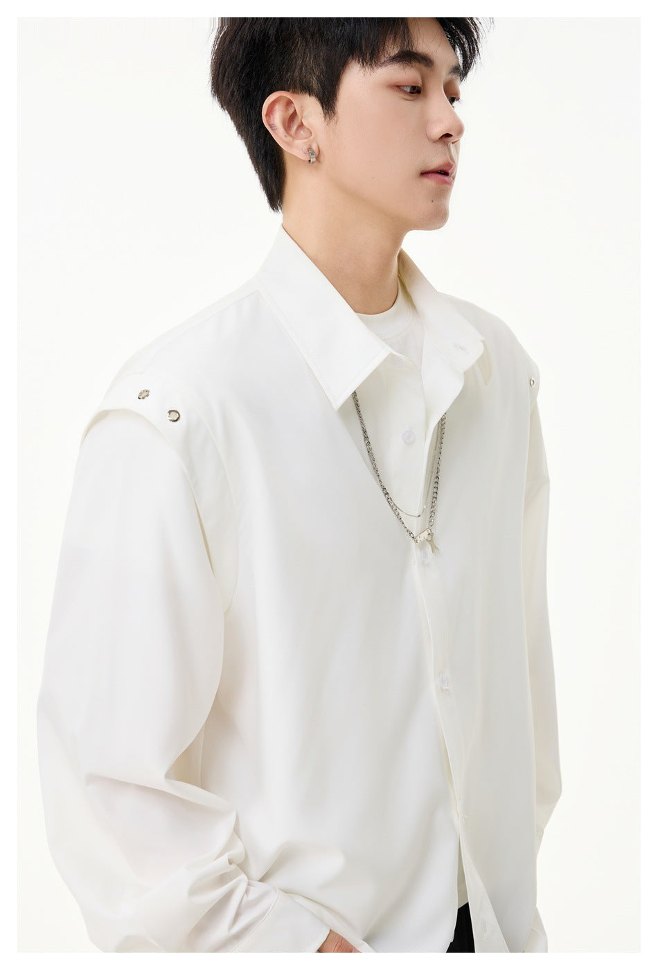 Close-up of a model wearing a white button-up shirt, showing its collar, shoulder snaps, buttons, and layered silver chain.