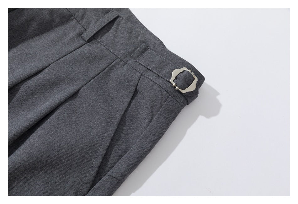 Close-up of charcoal gray trouser waistband with belt loops, pleats, and a silver side-adjustment buckle.