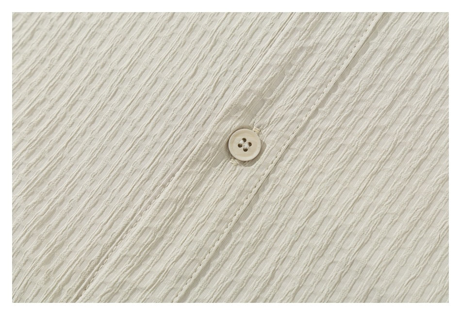 Close-up of a cream textured shirt fabric with a small four-hole button.