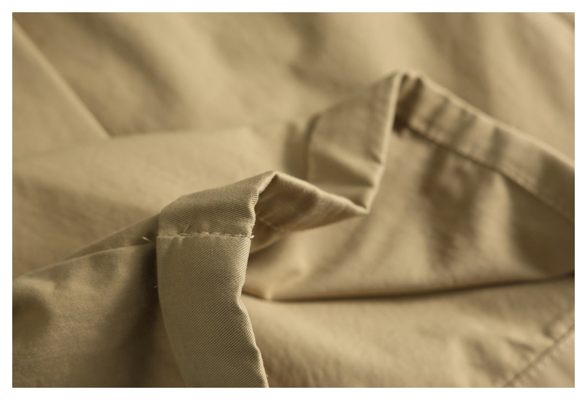 Macro view of tan garment fabric with a folded seam and visible topstitching.