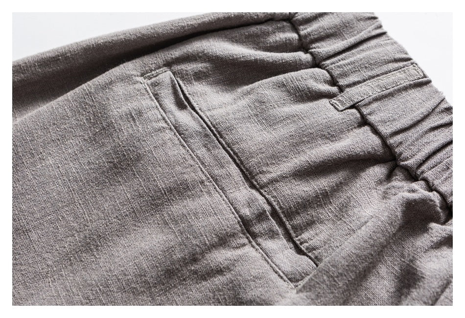 Close-up of gray trousers showing a stitched pocket opening beside the gathered elastic waistband.