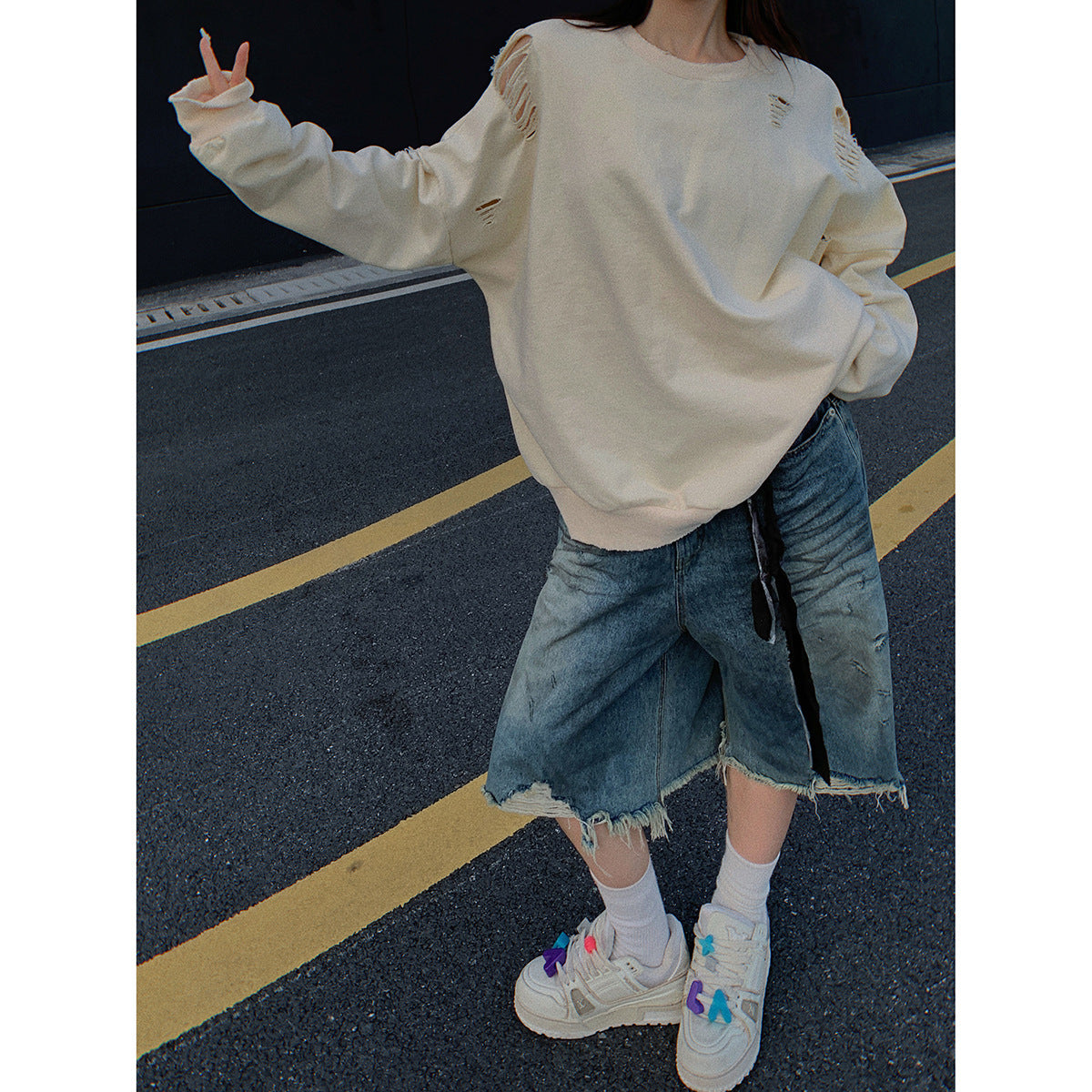Close view of a model wearing an oversized cream sweatshirt with distressed shoulder and sleeve details and frayed denim