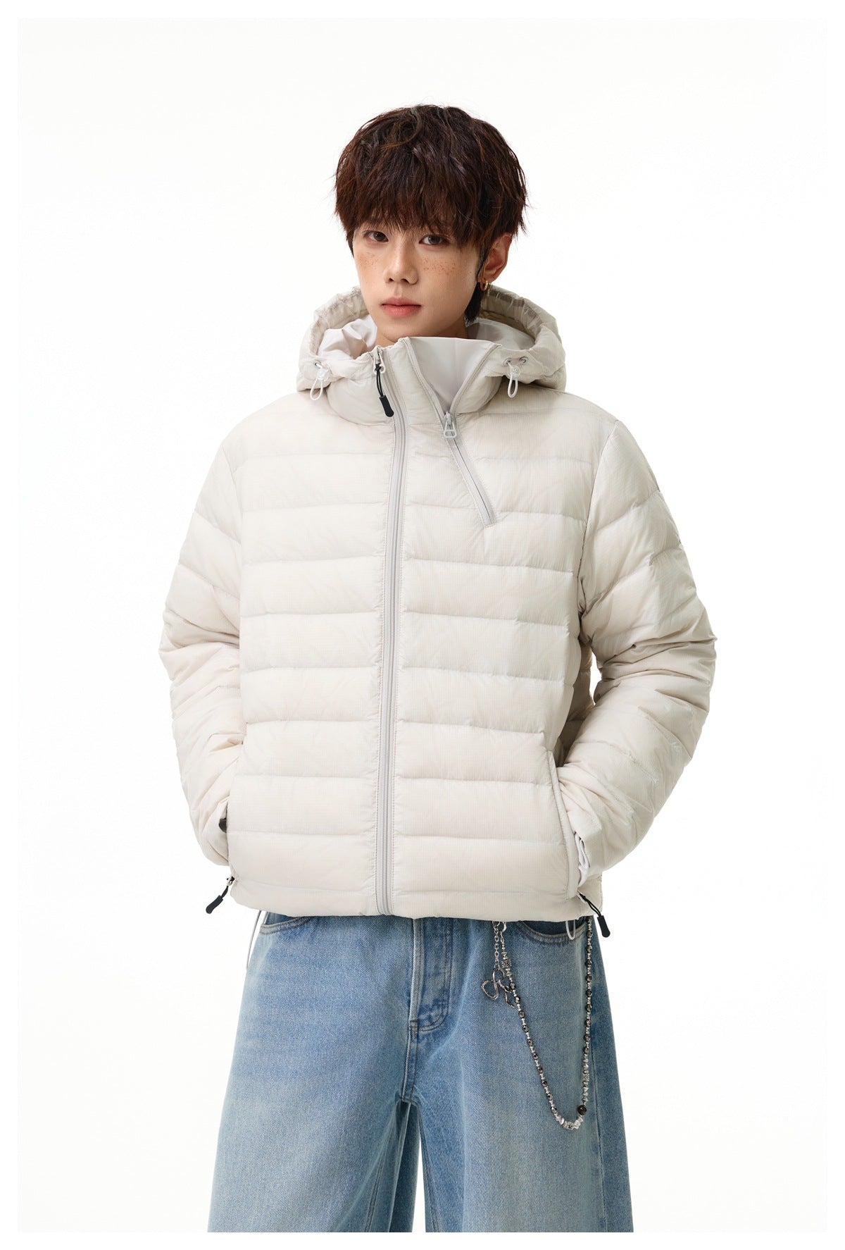 Model wearing an ivory hooded puffer jacket with an asymmetrical front zipper and light blue jeans.