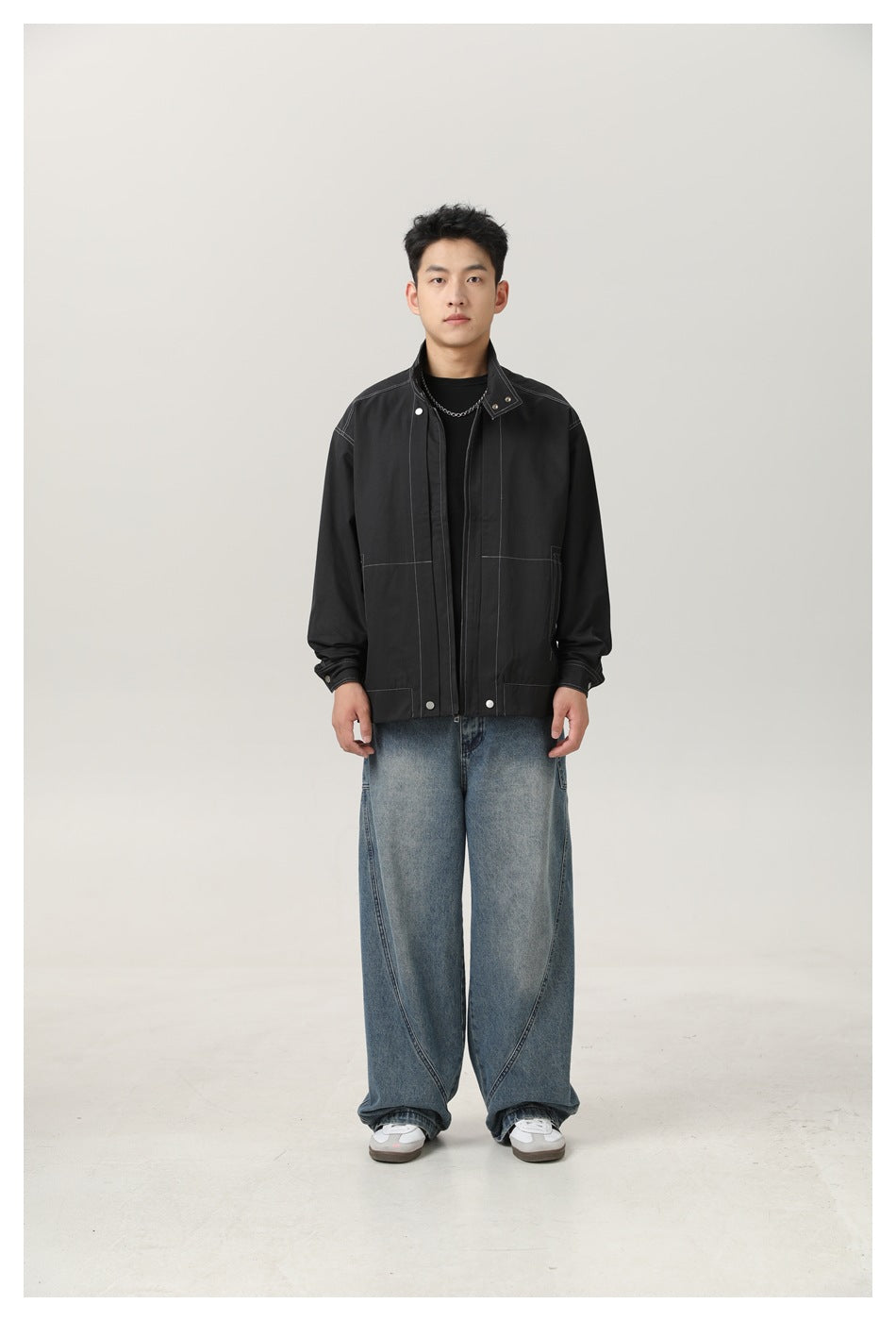 Man wearing black stand-collar zip jacket with white topstitching, front view, with wide-leg jeans