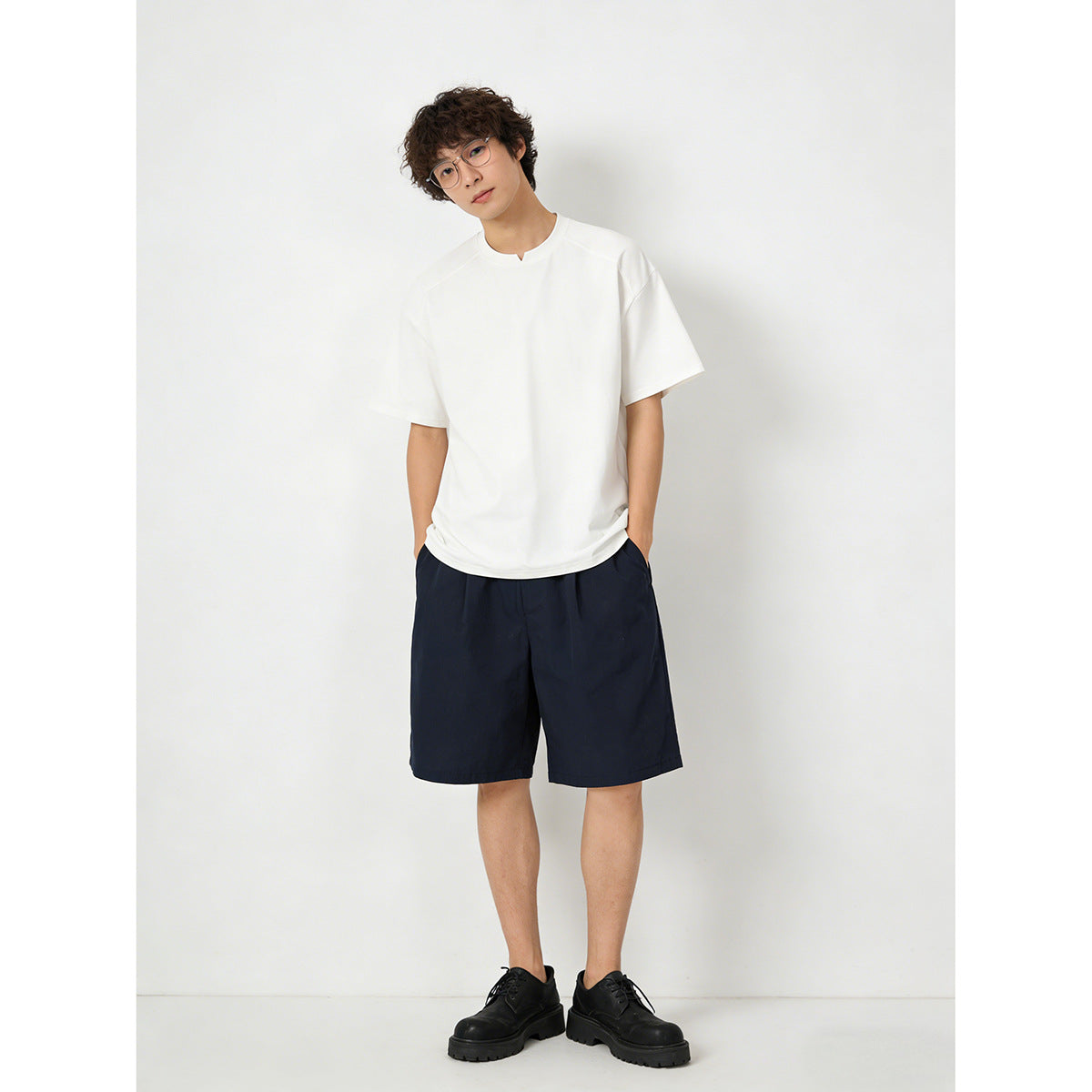 Model wearing a plain white short-sleeve crew-neck T-shirt with a small center neckline notch and navy shorts.