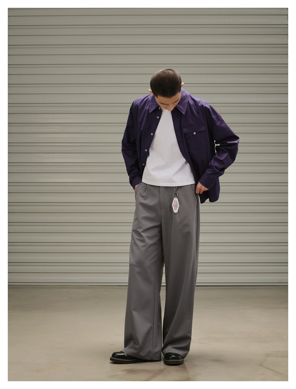 Model looking down, hands in pockets, wearing gray wide-leg pleated trousers with a purple shirt and white tee