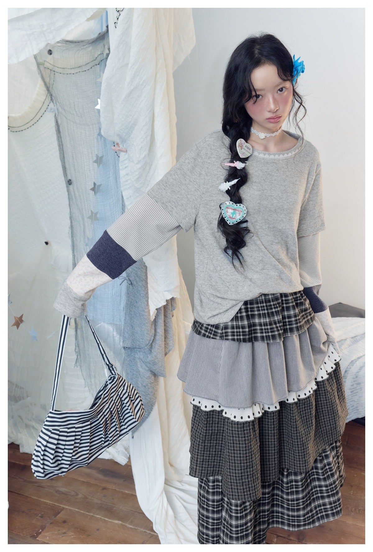 Model wearing a gray top with striped patchwork sleeves and a long layered dark plaid skirt.