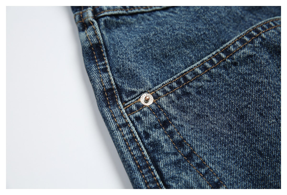 Close-up of blue jeans showing a metal rivet, diagonal seams, and golden-brown stitching.
