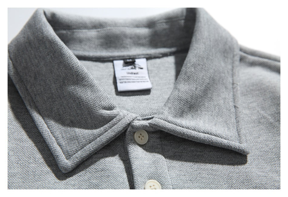 Close-up of the gray pullover's pointed collar, top button, textured fabric, and inner neck label.