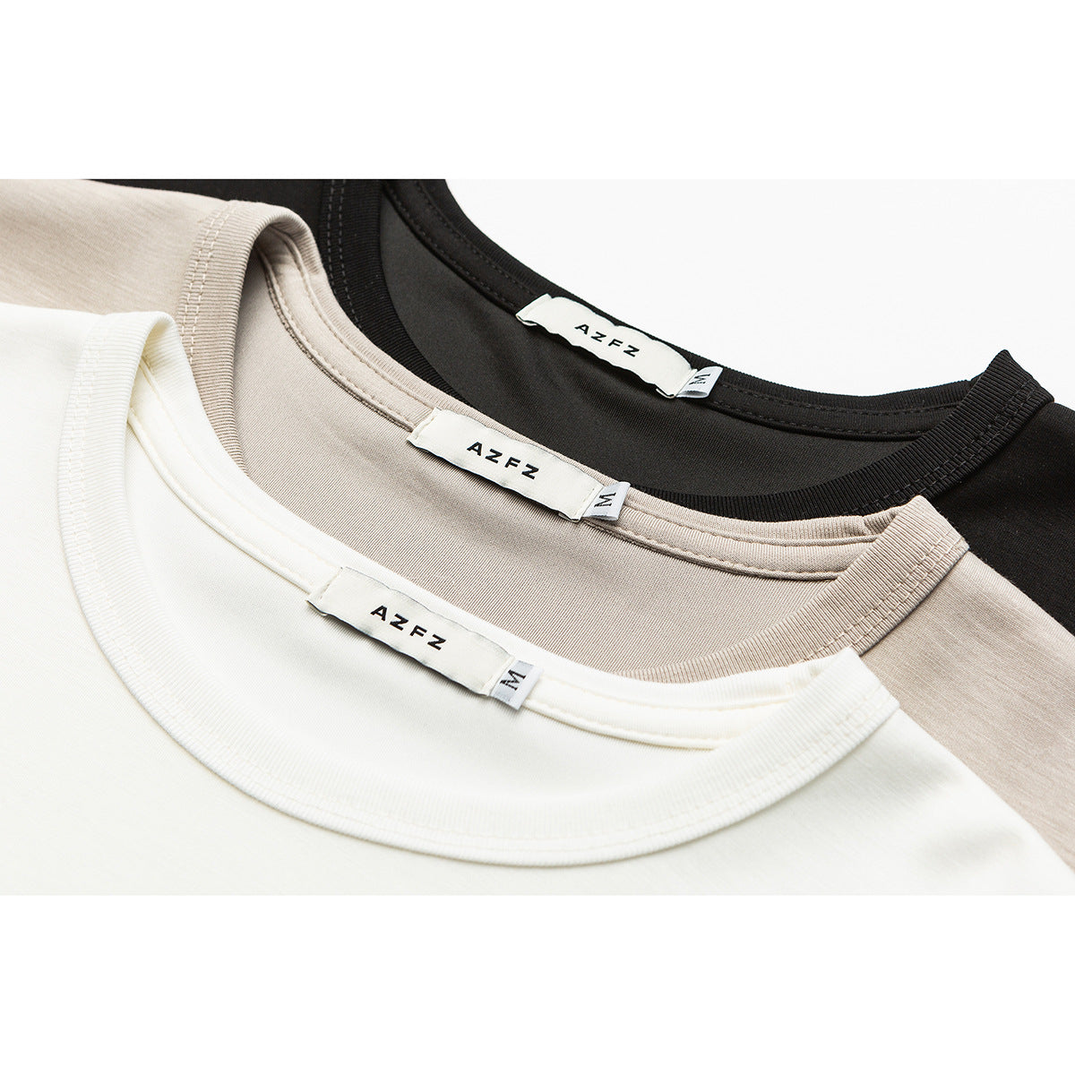 Close-up of white, beige, and black T-shirt necklines with ribbed crew collars and sewn-in labels.