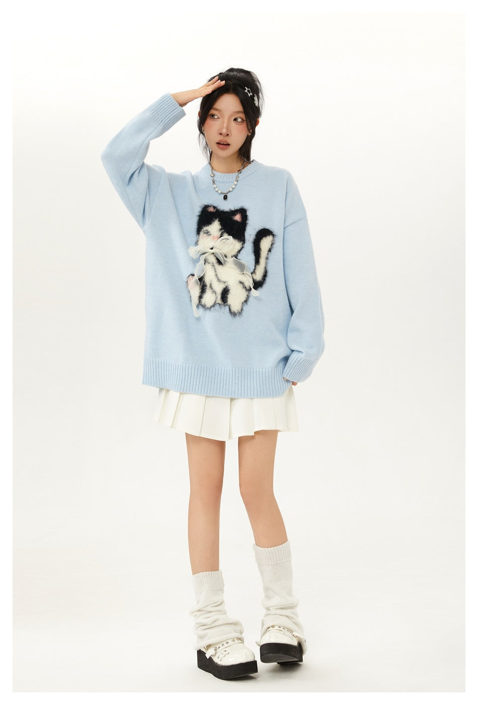 Woman in light blue cat sweater with one hand raised to forehead, white pleated skirt and leg warmers